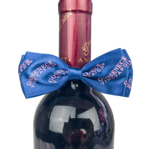 Blue bow tie with pink logo displayed on the neck of a wine bottle
