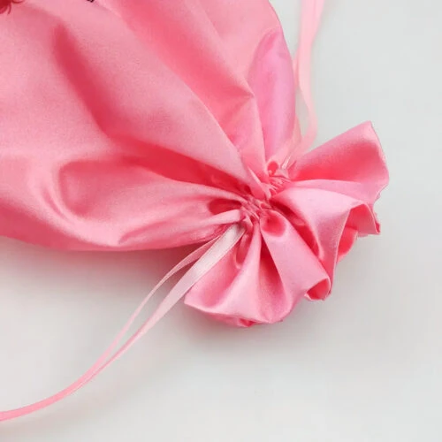 صورة مقربة لقسم الرباط في حقيبة ساتان وردية اللون مطبوع عليها اسم العلامة التجارية للعميل والبريد الإلكتروني وحساب إنستغرام وفيسبوك. الحقيبة مزينة بصورة ظلية لامرأة ذات شعر جميل.