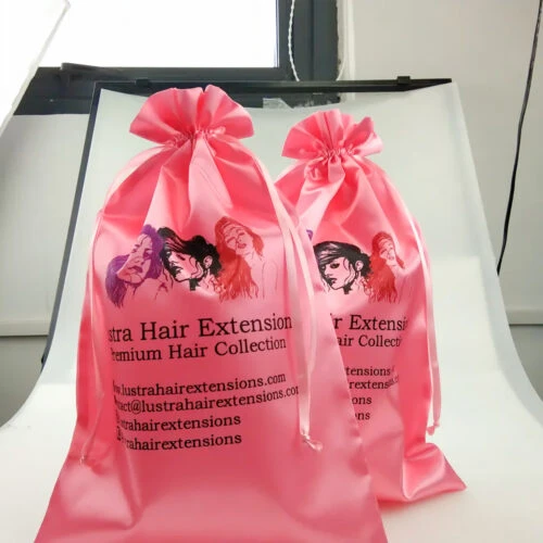 حقيبتان ورديتان مملوءتان بسلك سحب من الساتان مطبوع عليهما اسم العلامة التجارية للعميل والبريد الإلكتروني وإنستغرام وفيسبوك. يتم عرض الحقائب في وضع مستقيم.