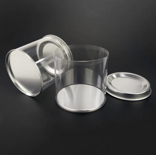 Plastic tube with tin lid standing upright and plastic tube with tin lid lying horizontally, with the lid of the upright tube open and placed aside.