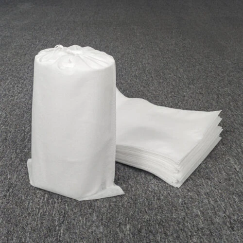 حقيبة غبار مخصصة غير منسوجة مع رباط محكم، واقفة ومملوءة، إلى جانب كومة من أكياس الغبار غير المستخدمة خلفها.