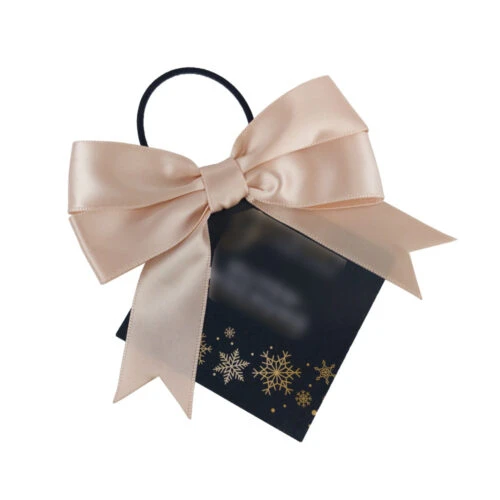 Elegante lazo doble personalizado en color crema sobre una bolsa de regalo negra adornada con copos de nieve dorados.