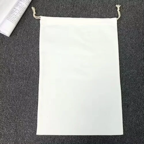 カスタマイズ可能な白い巾着袋。ロゴ印刷の準備ができており、灰色の表面に平らに置かれています。