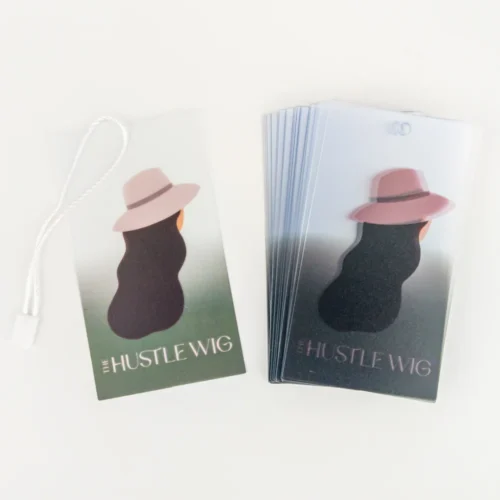 UV 印刷によるカスタム透明 PVC ハングタグ。帽子をかぶった人物のシルエットと「#HUSTLEWIG」の文字が描かれています。タグは小ロット注文に適しており、角が丸くなっています。