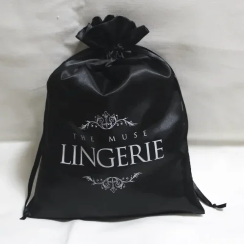 Bolsa de cordón negra personalizada con logo impreso en blanco y elementos decorativos, fabricada en seda poliéster 100% con superficie lisa.