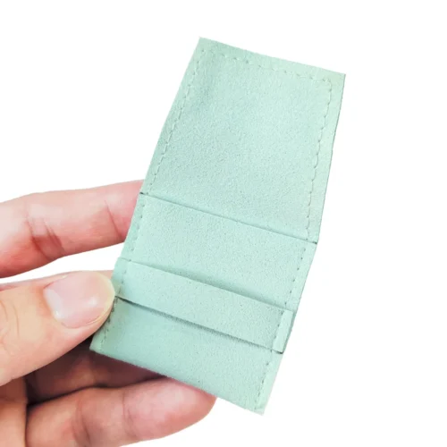 A hand holding a custom microfiber suede ring pouch in a light green color, exemplifying the product’s design and texture.