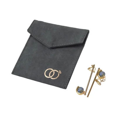 Custom black velvet jewelry bag with metallic circle clasp next to gold-toned earrings with blue gemstones.