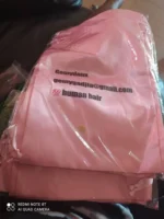 A pink drawstring bag with the printed text gmail and “100% human hair,” along with a small circular sticker with Asian characters.