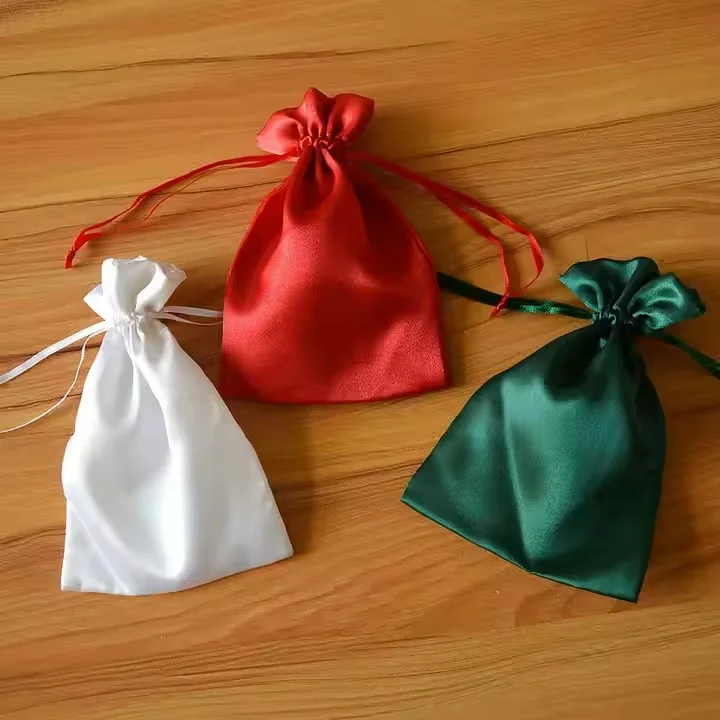 Bolsas de regalo con cordón personalizables en blanco, rojo y verde colocadas sobre una superficie de madera.