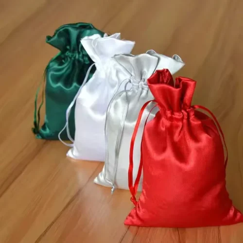 Customizable satin drawstring gift pouches in green, white, and red on a wooden surface.