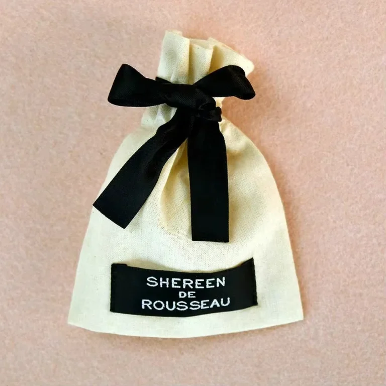 حقيبة مخصصة برباط مصنوعة من قماش طبيعي، تتميز بشريطة سوداء وعلامة قماشية للعلامة التجارية.