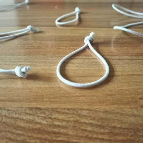 Auf einer Holzoberfläche werden individuelle elastische Schnurschlaufen angezeigt, die Flexibilität und verschiedene Stile für Etiketten oder Bündelung demonstrieren.