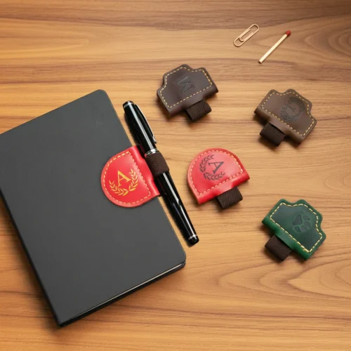 Des échantillons de marque-pages magnétiques en cuir sont présentés avec un carnet et un stylo sur un bureau en bois.