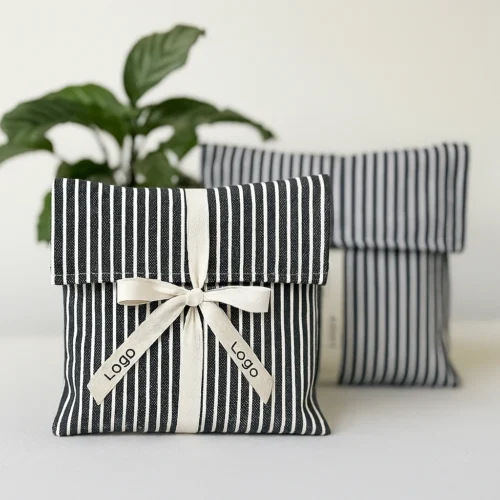 Front-view sample of cream custom fold over pouches with black ribbon ties on a white background.