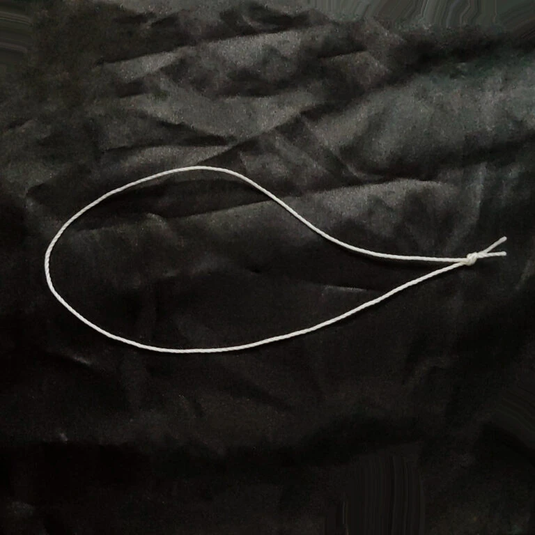 Pre-Tied Tufting Loops, a white 3-strand nylon loop with a tight end knot resting on dark upholstery fabric ready for Chesterfield button tufting.