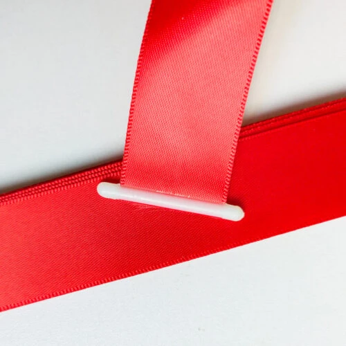 Close-up of a ribbon with plastic end stopper, the white T-bar lying flat across the ribbon end on a red satin band.