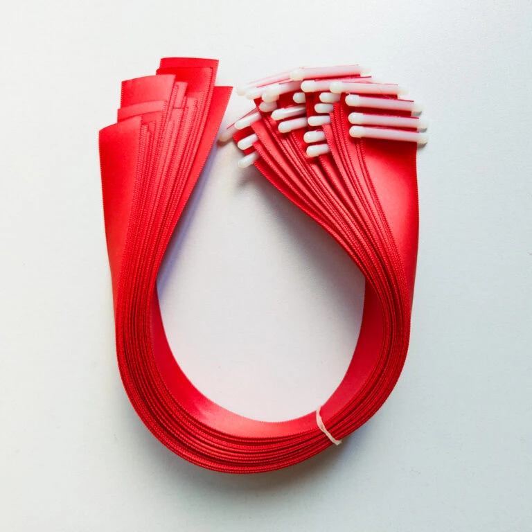 Bulk red satin ribbon with plastic end stopper fitted to each cut length, bundled for packing.