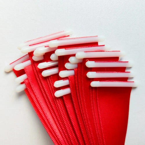 Close-up of a red satin ribbon with plastic end stopper, showing the white T-bar seated at the ribbon end.