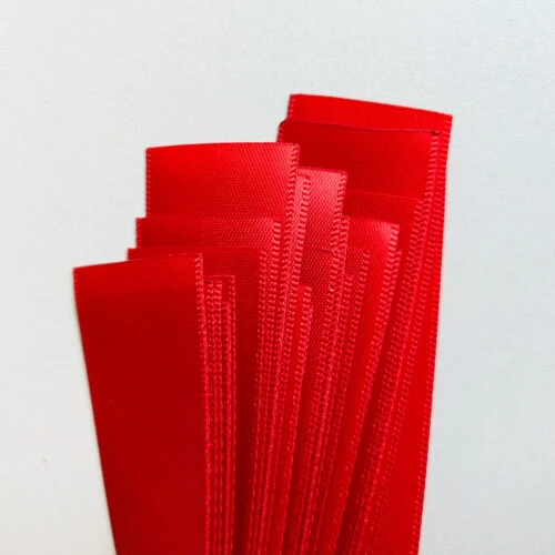 Red satin ribbon stock for a custom ribbon with plastic end stopper order, cut to matched lengths.