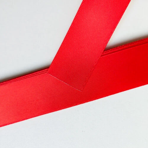 Stitched end fold on a red satin ribbon with plastic end stopper, forming the pocket for the plastic bar.