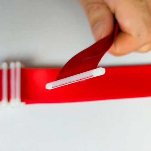 Hand holding a ribbon with plastic end stopper in a loop, white T-bar visible at the base.